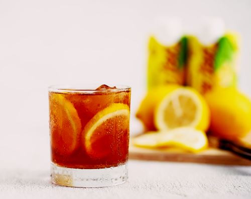 glass with ice tea and lemon slice in it, lemons to the upper right behind glass