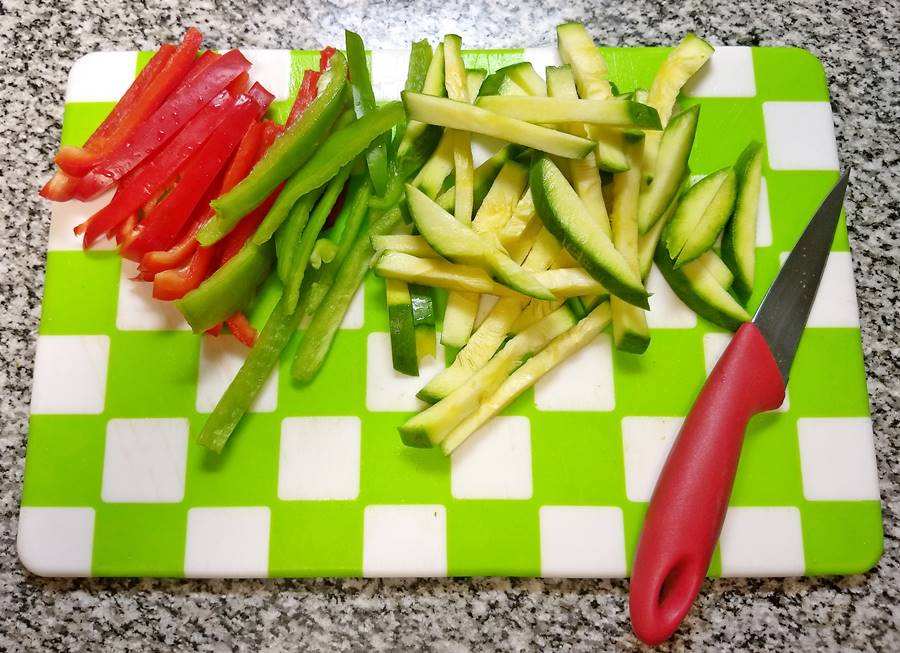 sliced red and green peppers and green summer squash on board