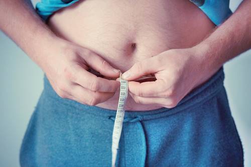 man measuring waistline with tape measure