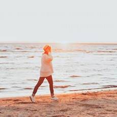 woman walking along a sandy beach, by calm ocean at sunset