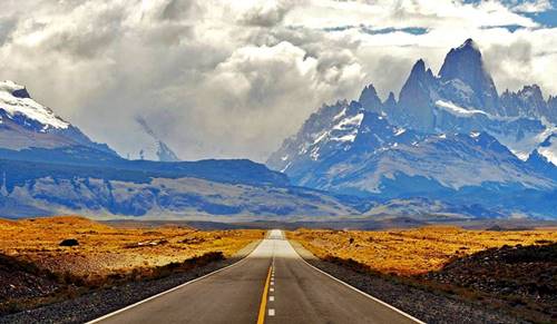 snowcapped steep mountains in Patagonia, seen from the highway leading to them in the steppe, cloudy sky