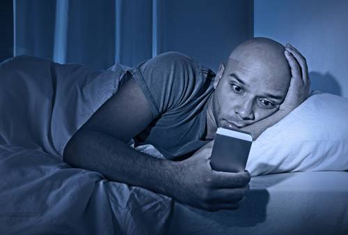 man awake at night watching his mobile phone bathed in blue light