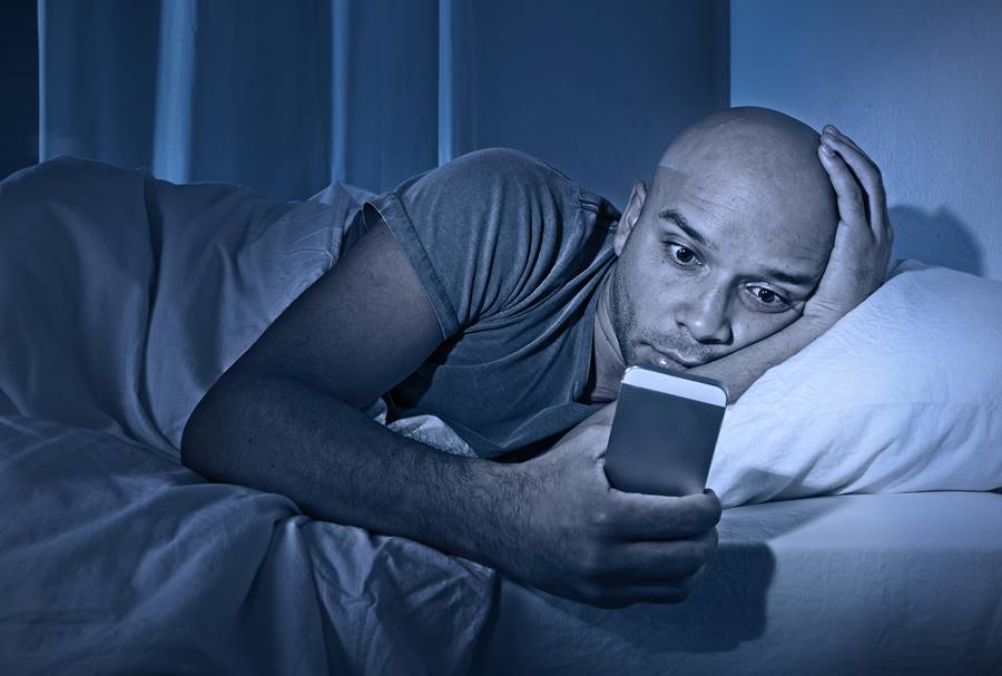 man awake at night watching his mobile phone bathed in blue light