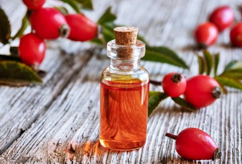 red rose hips on a wood surface and a small vial with red tinted oil